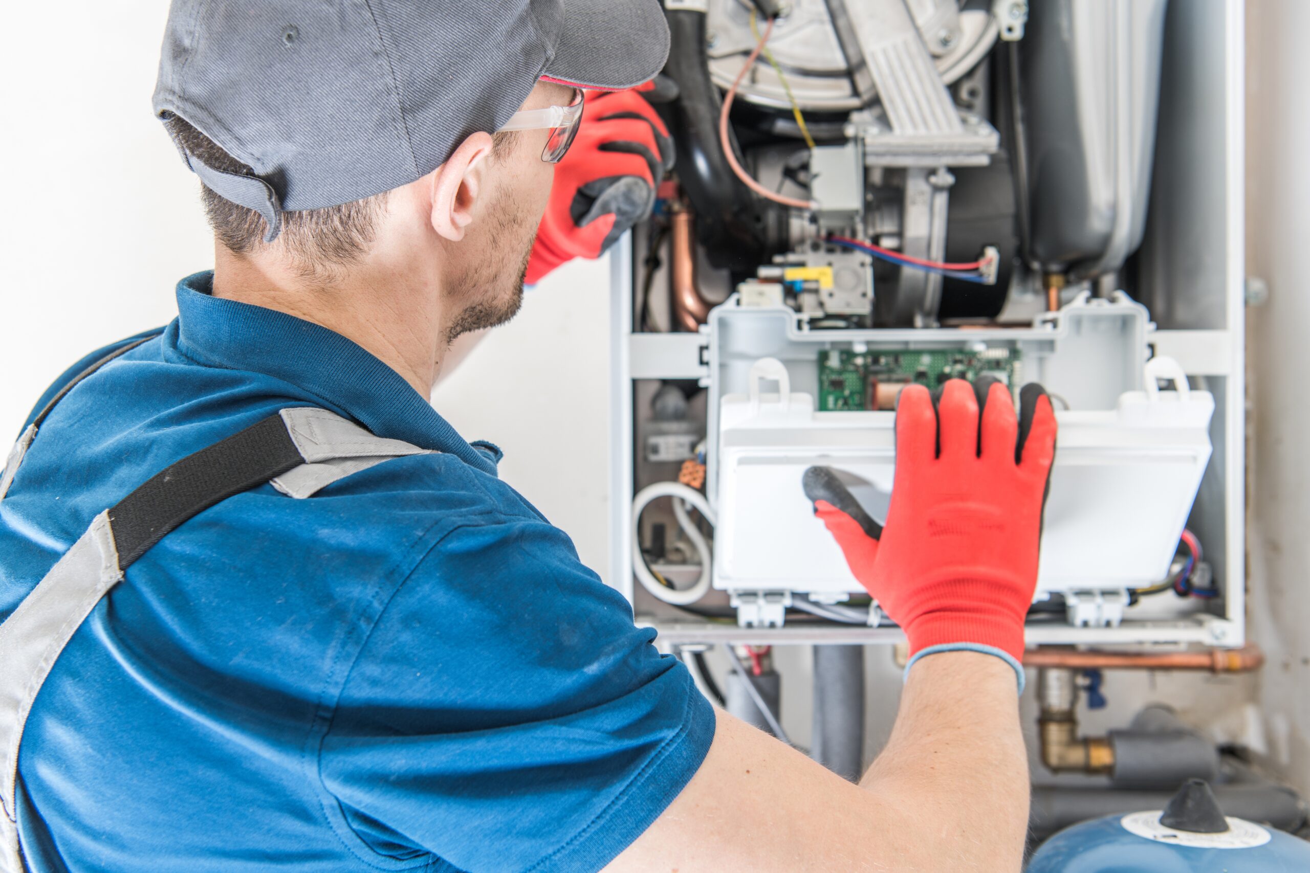 A technician in a blue shirt and red gloves is troubleshooting a gas furnace