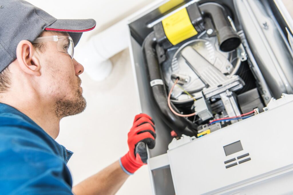 A man wearing a blue shirt and red gloves repairs a gas furnace