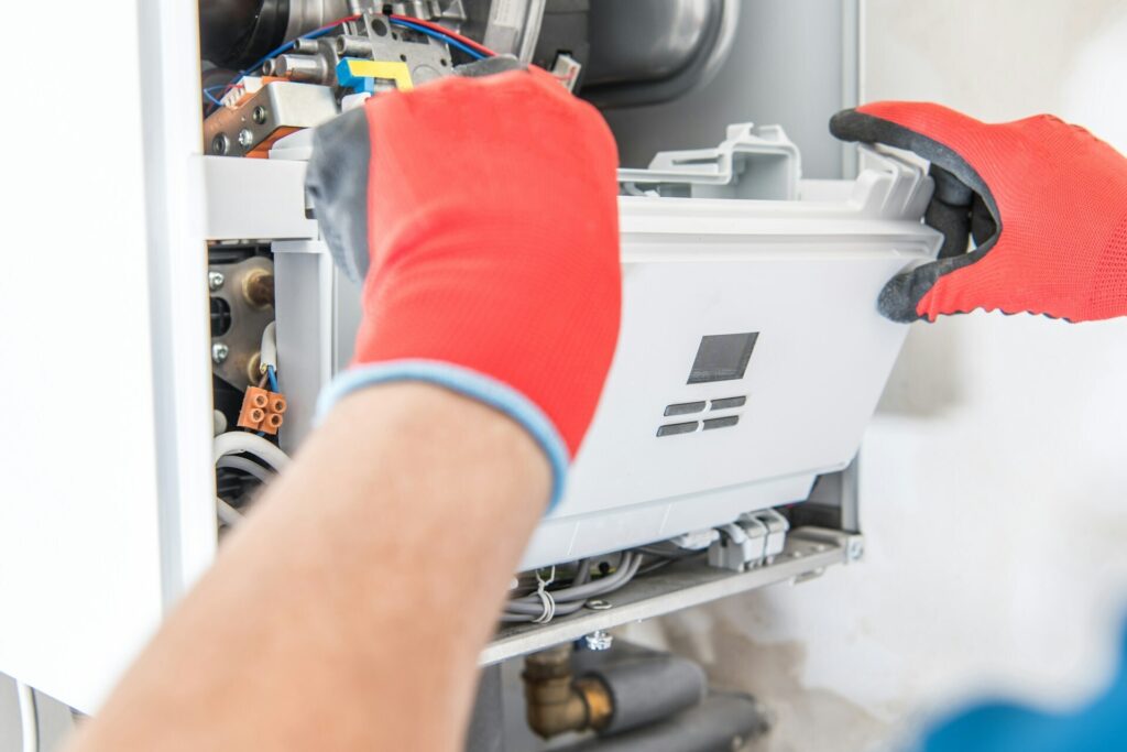 A technician in red gloves is fixing a gas boiler