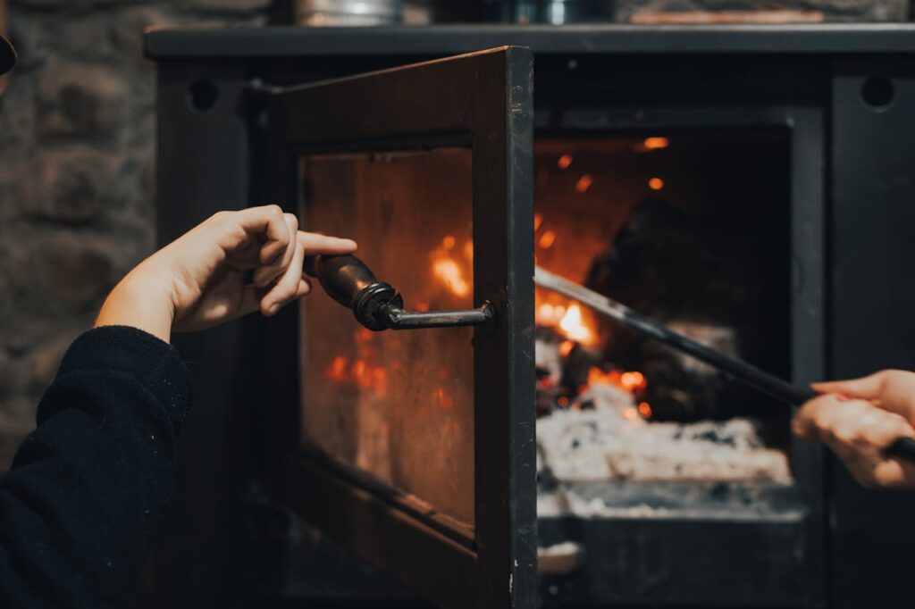 A woman is using a tool to open the door of a wood-burning stove