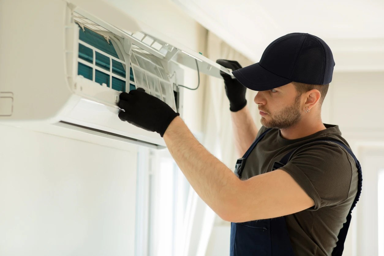 A man in a hat and gloves is adjusting an air conditioner